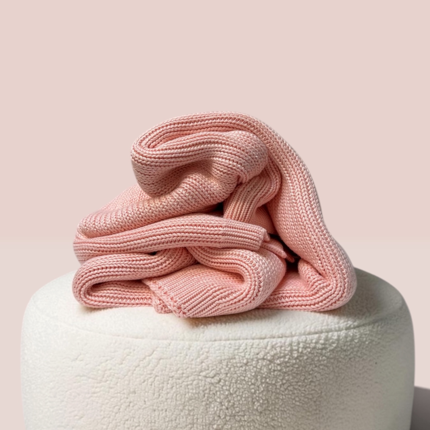 Kids bamboo weighted blanket in Rosewater Pink draped on top of a round white textured ottoman against a solid pale pink background.