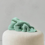 A soft, pale sage green ribbed knit kids weighted blanket artfully folded on top of a round cream bouclé ottoman against a neutral background. 2.2kg for children around 22kg to 30kg.